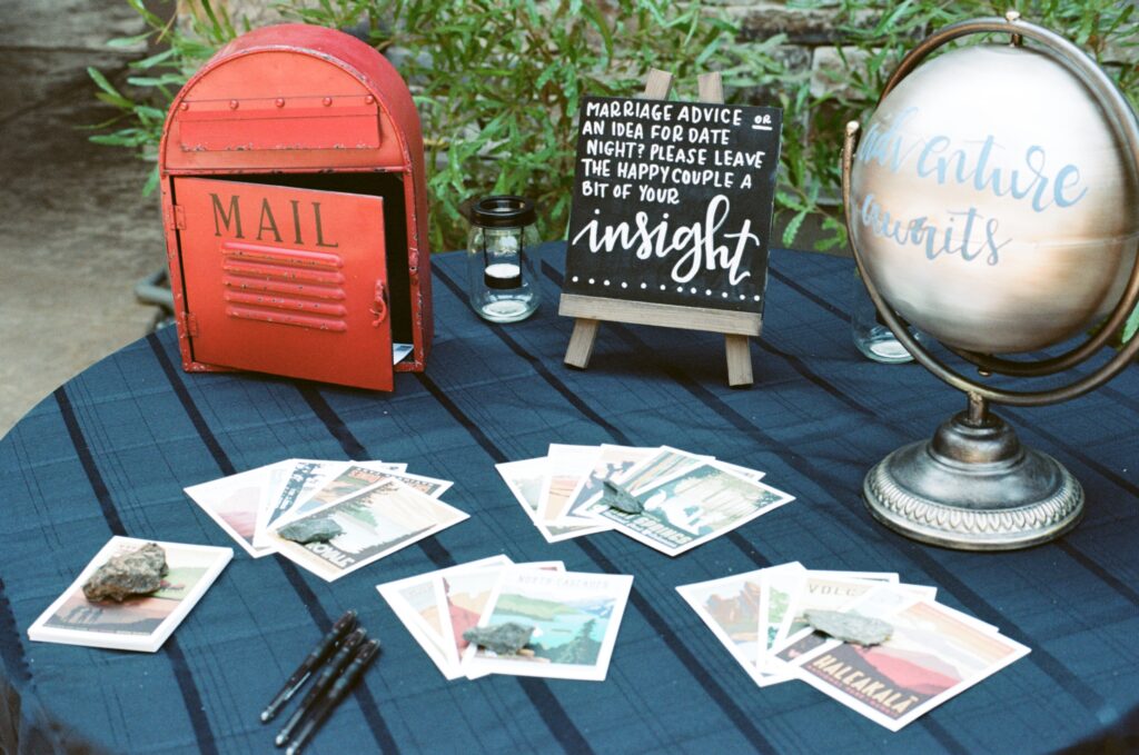 A welcome table at a wedding weekend featuring a blue tablecloth, red mailbox, wedding sign, globe, and postcards.